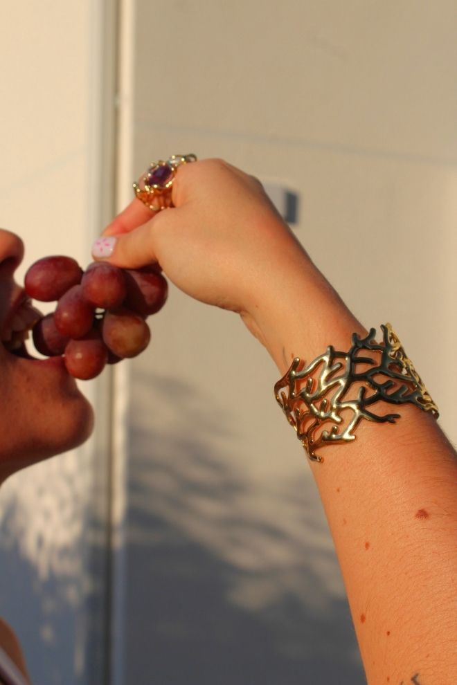 Brazalete Arrecife Tico lucido en la muñeca mientras se sostiene un racimo de uvas