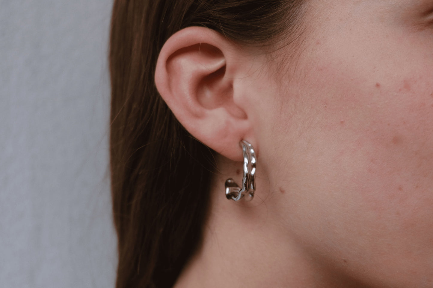 Pendientes plateados "The Spark Drop" lucidos por una modelo con pelo recogido.