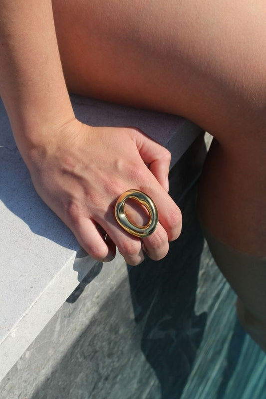 El Anillo Carambola en una mano junto a una piscina, resaltando su brillo y forma escultórica.