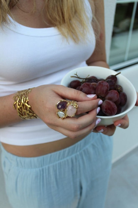 Mujer sosteniendo un cuenco de uvas mientras luce el Anillo Costa Violeta con piedras llamativas.