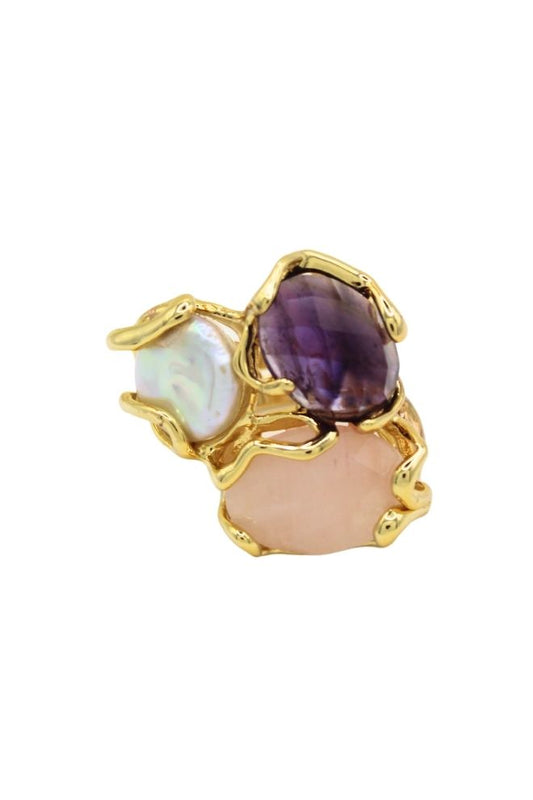 Anillo Costa Violeta con tres piedras en tonos violeta, rosa y blanco sobre estructura dorada.