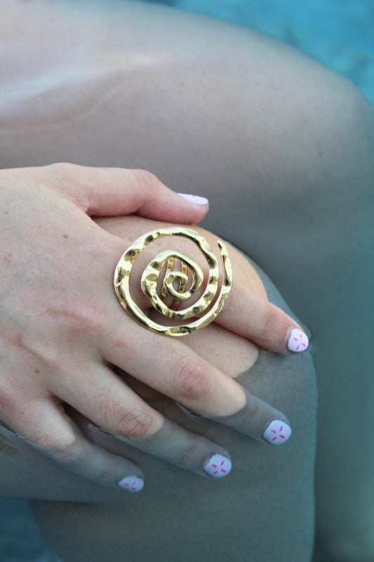 Anillo Espiral Maracuyá en mano junto a la piscina, destacando su brillo dorado.