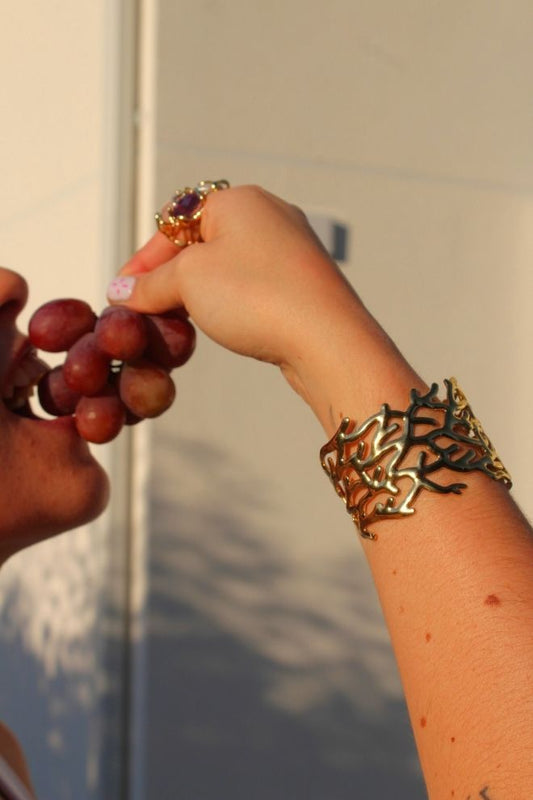Brazalete Arrecife Tico lucido en la muñeca mientras se sostiene un racimo de uvas
