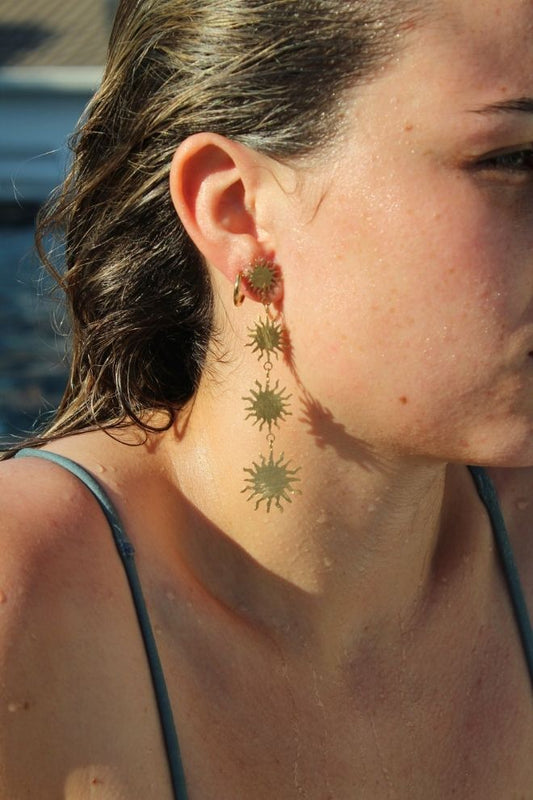 Modelo luciendo los Pendientes Rayitos, largos y dorados, con forma de sol.