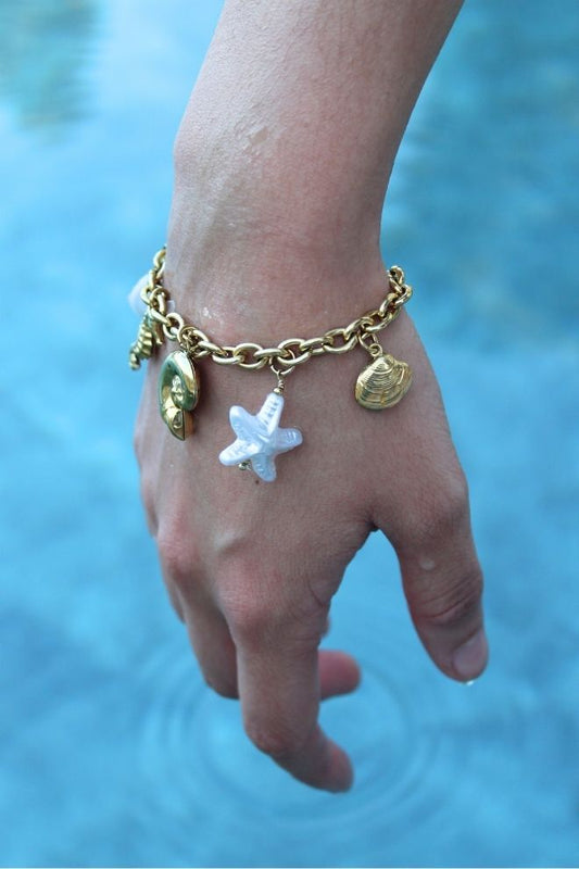 Persona luciendo la Pulsera Arena y Sol frente a una piscina, destacando sus charms veraniegos.